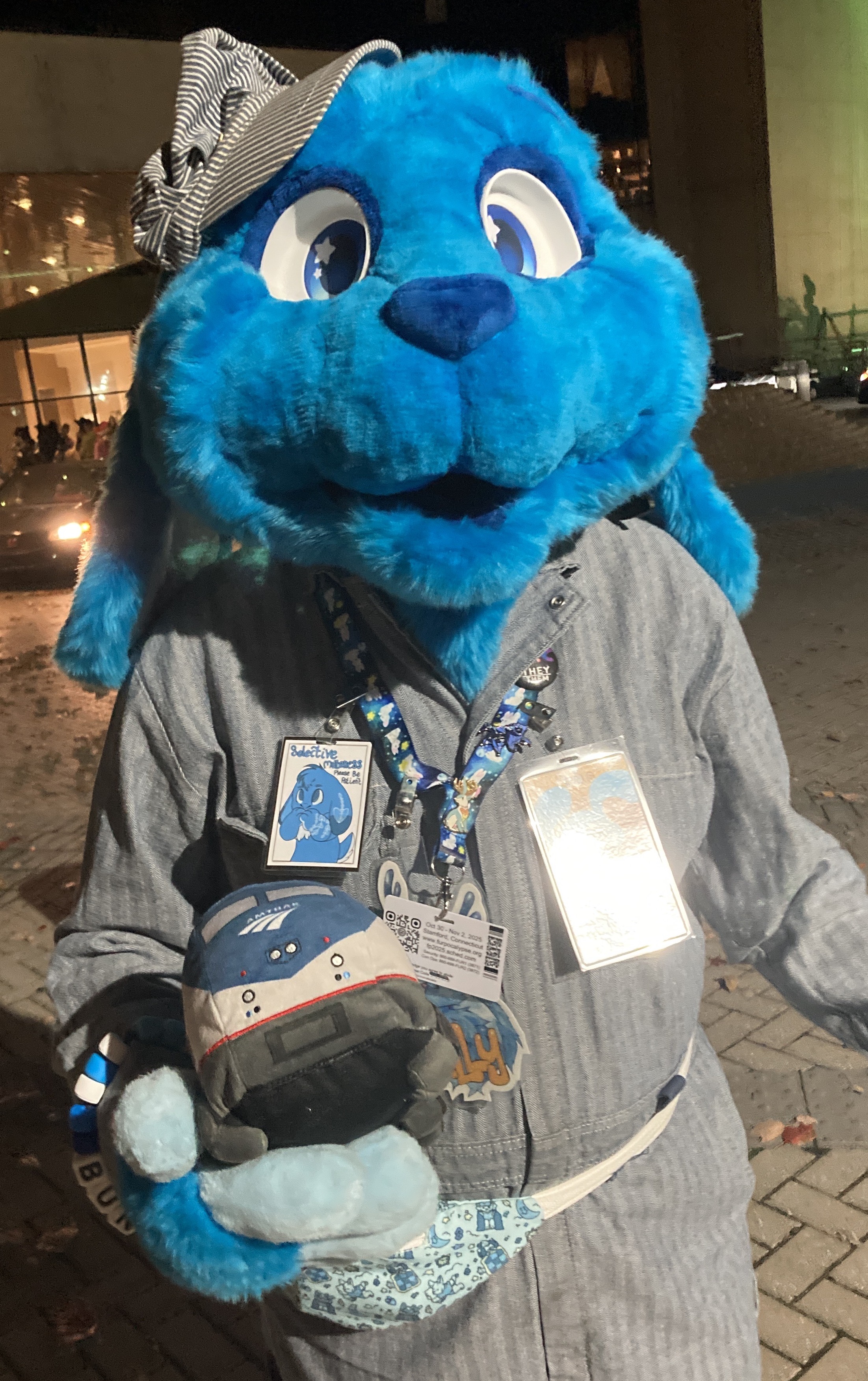 A blue bunny fursuiter wearing a train conductor uniform and holding a plush locomotive
