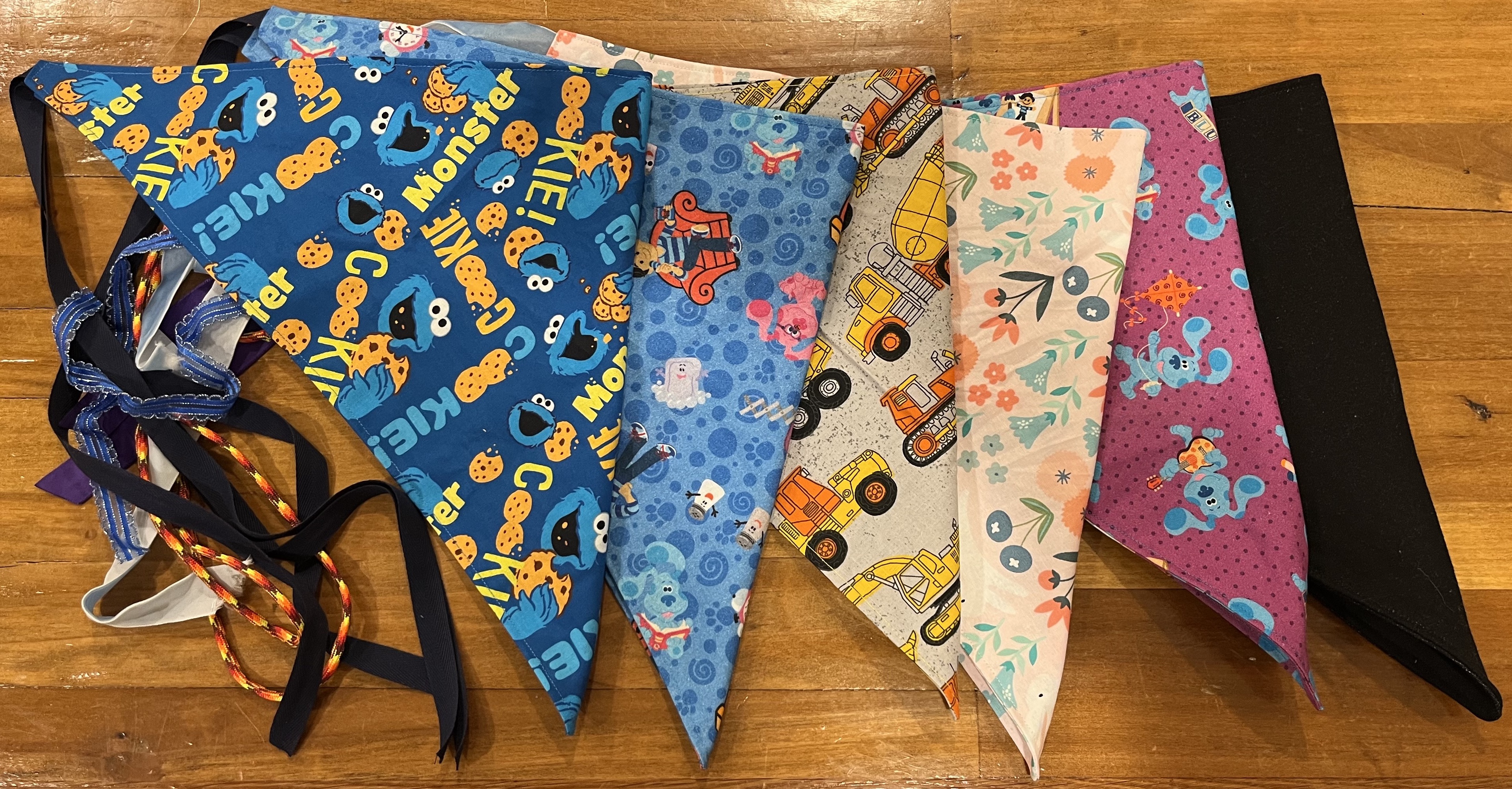 Five fursuit bandanas, in Cookie Monster print, Blue's Clues print on blue, construction print, pink bunny print, Blue's Clues print on purple, and solid black
